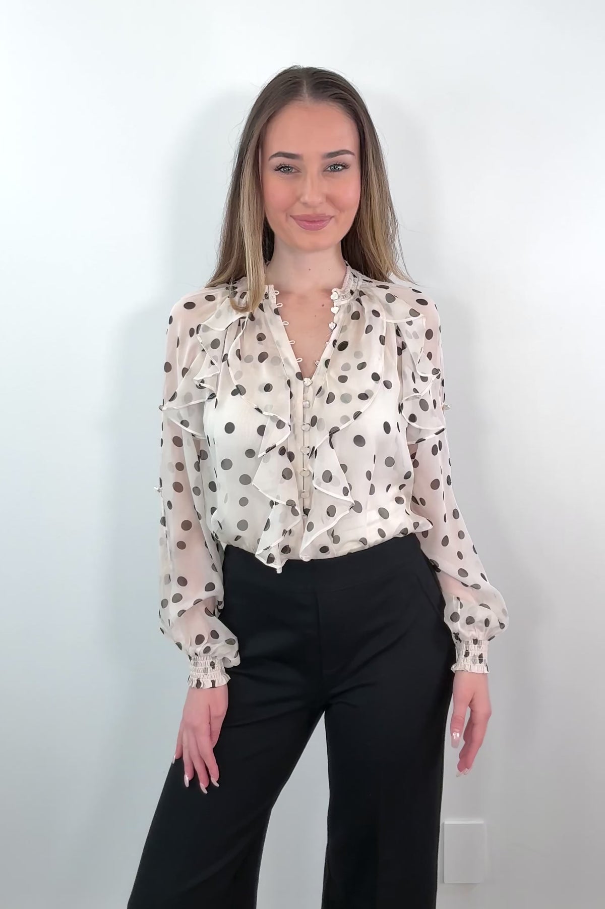 video of a Woman wearing a sheer ruffle blouse with polka dots tucked in