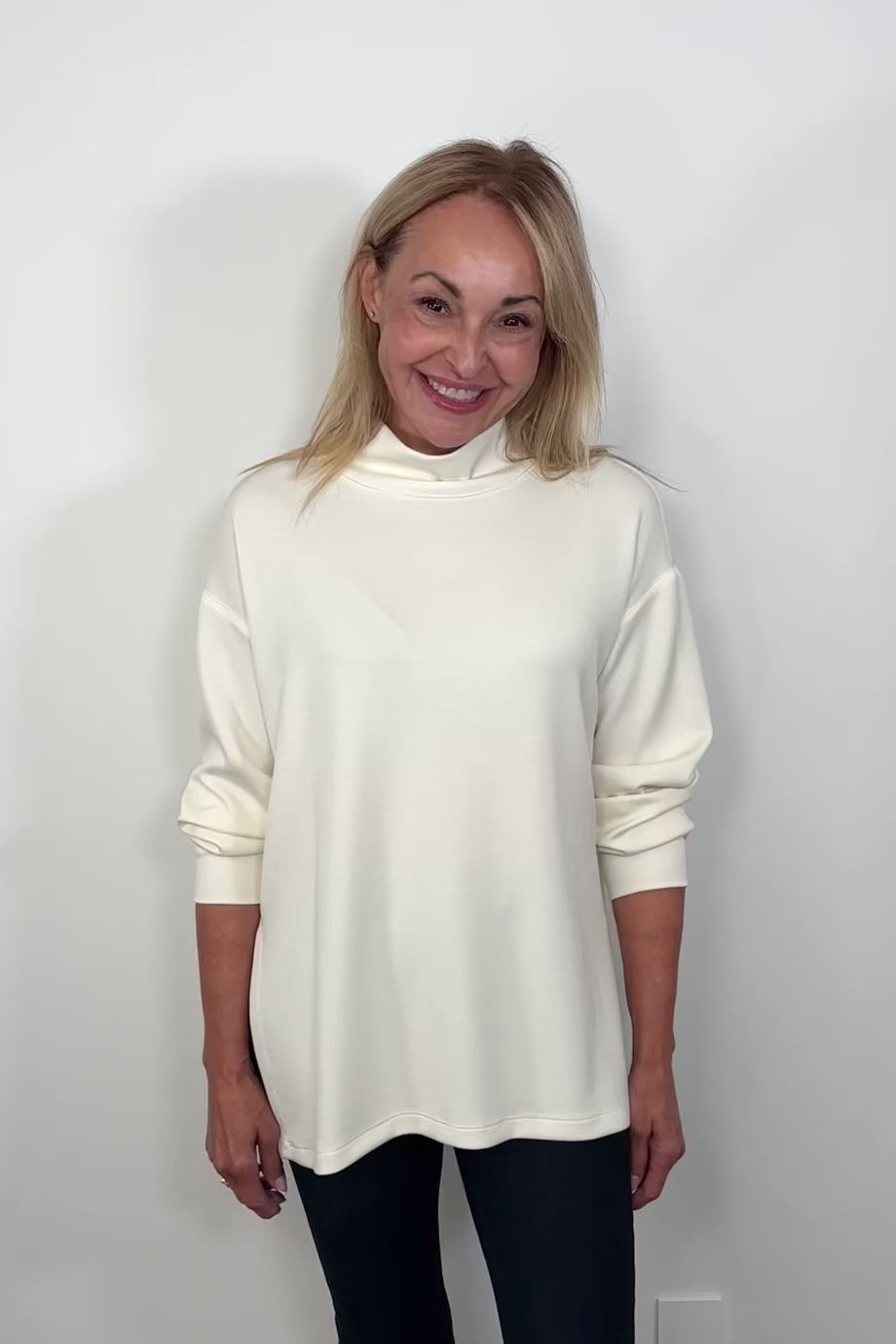 Video of a woman wearing a white boxy turtleneck top turning around to show the back