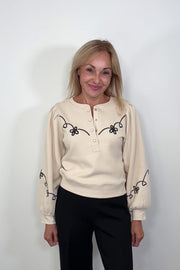 Video of a woman wearing a ecru coloured sweatshirt with a western inspired detailing in the arms and chest turning around to show the back of the garment 