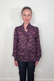 Video of a woman wearing a violet sheer printed blouse with ruffles untucked