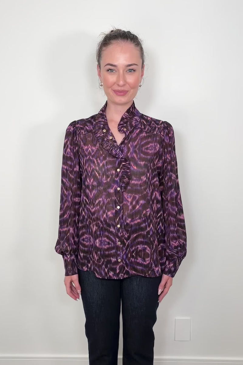 Video of a woman wearing a violet sheer printed blouse with ruffles untucked