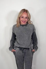 Video of a woman wearing a gray pullover sweatshirt with detailing on the sleeves