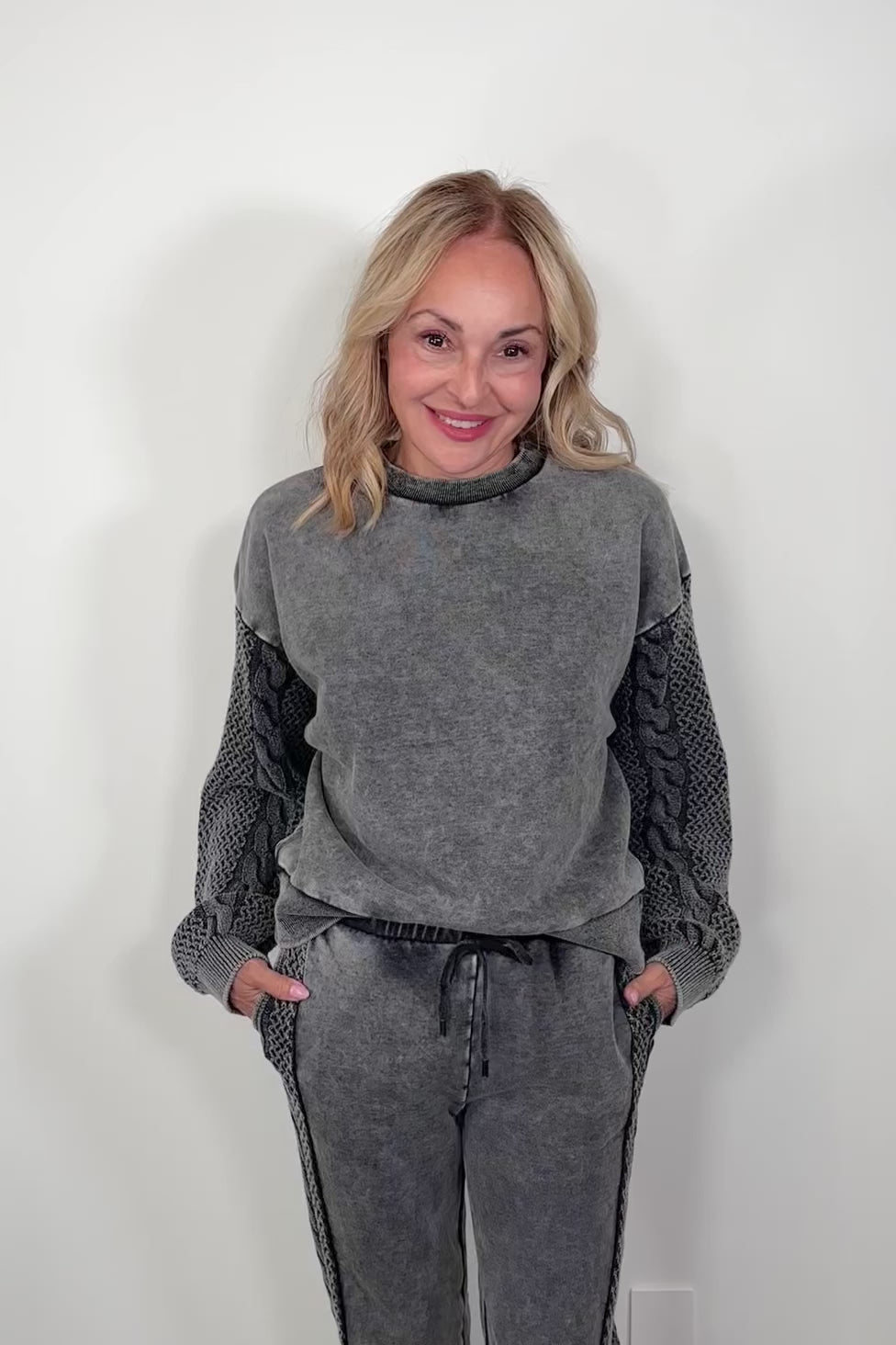 Video of a woman wearing a gray pullover sweatshirt with detailing on the sleeves