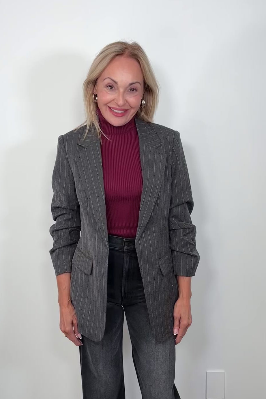 Video of woman wearing a burgundy turtle neck tank top layered with a gray pinstripe blazer with sparkles