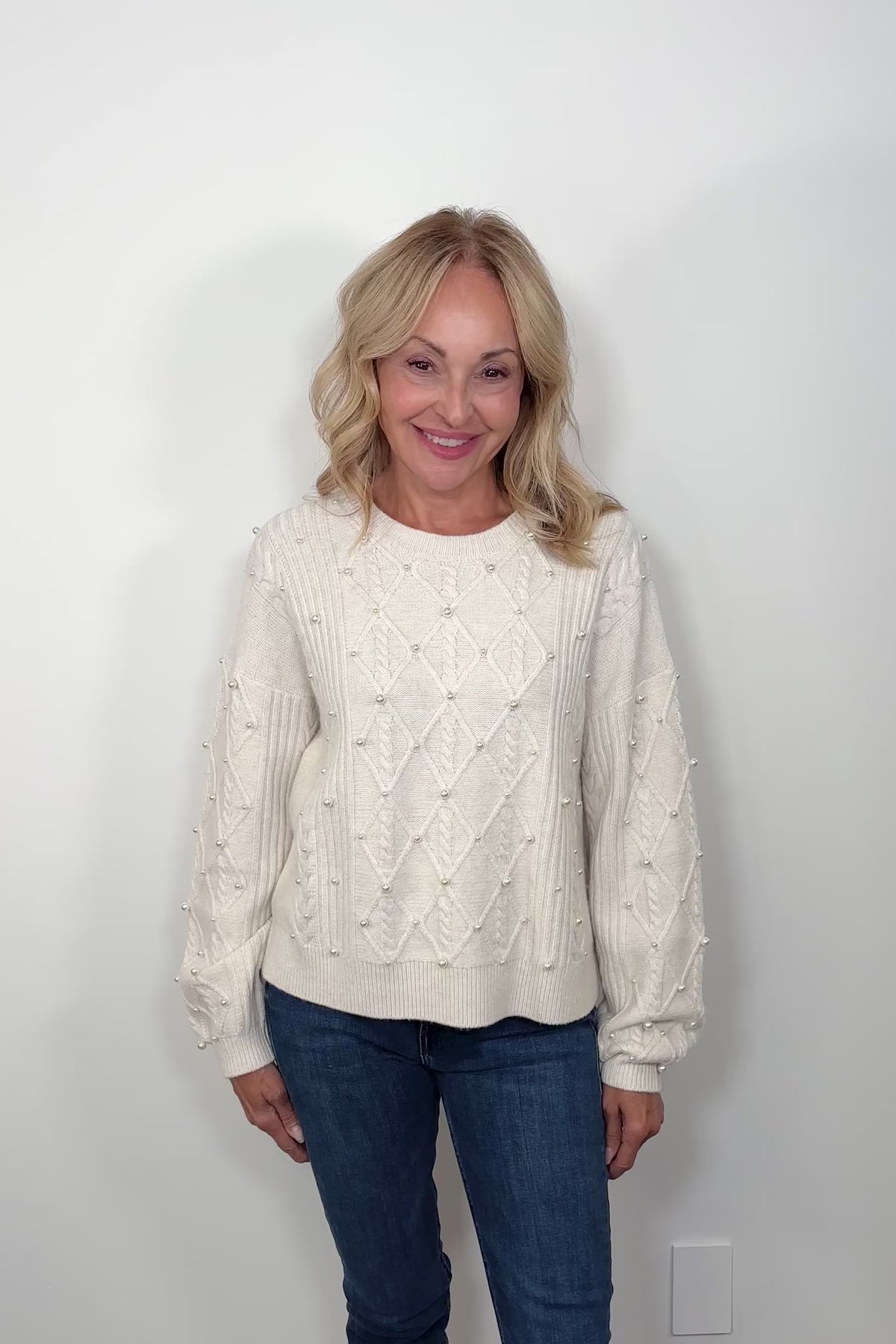 Video of a woman wearing a white sweater with pearl embellishments 