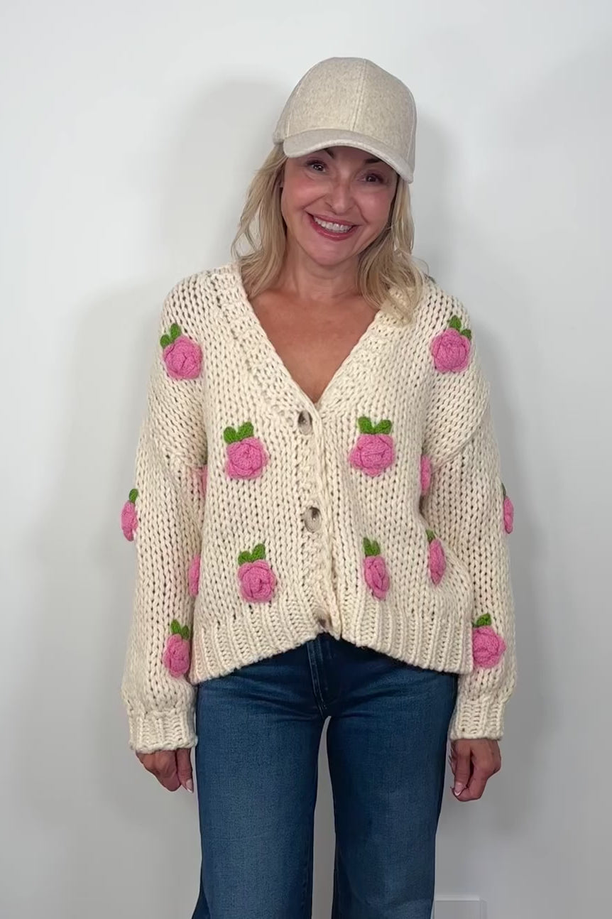 Video of woman wearing an off white sweater with pink roses and a V-neck turning around to show the back