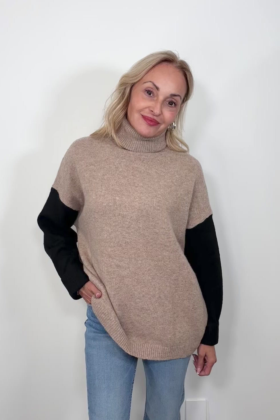 Video of woman wearing a beige turtle neck sweater with black sleeves and oat meal coloured back