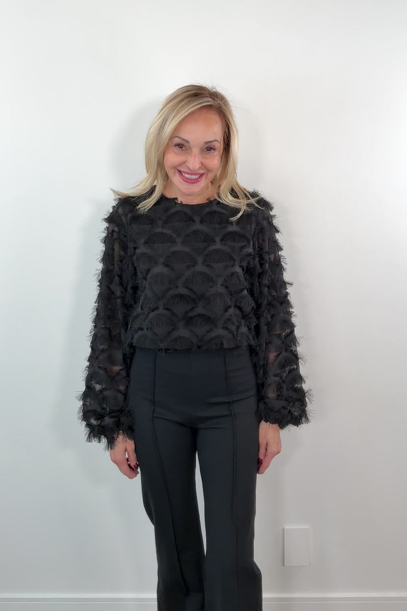 Video of a woman wearing a black top with sheer panels and frills