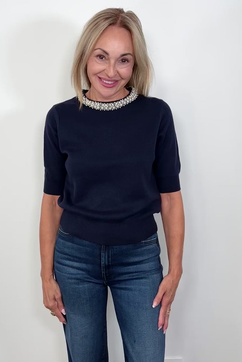 video of woman wearing a navy knitted top with pearl detailing in the neck