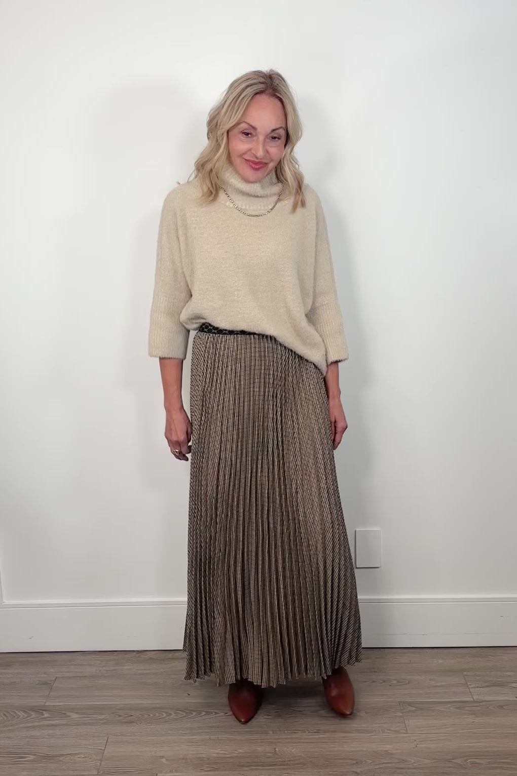 Video of a person wearing a long pleated skirt with a neutral background