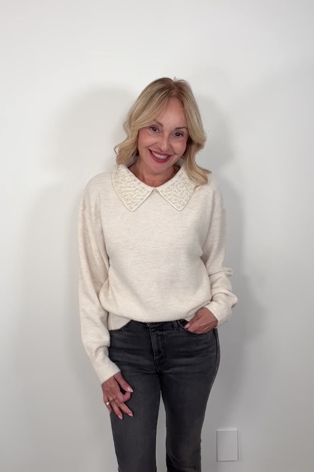 video of a woman wearing an off white collard sweater with pearl detailing 