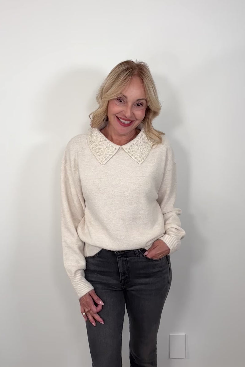 video of a woman wearing an off white collard sweater with pearl detailing 