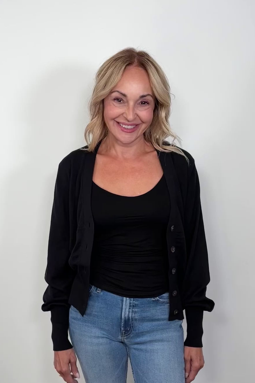 front facing woman wearing a black cotton, silk and cashmere blend cardigan with extended cuffs open turning around to show the back.
