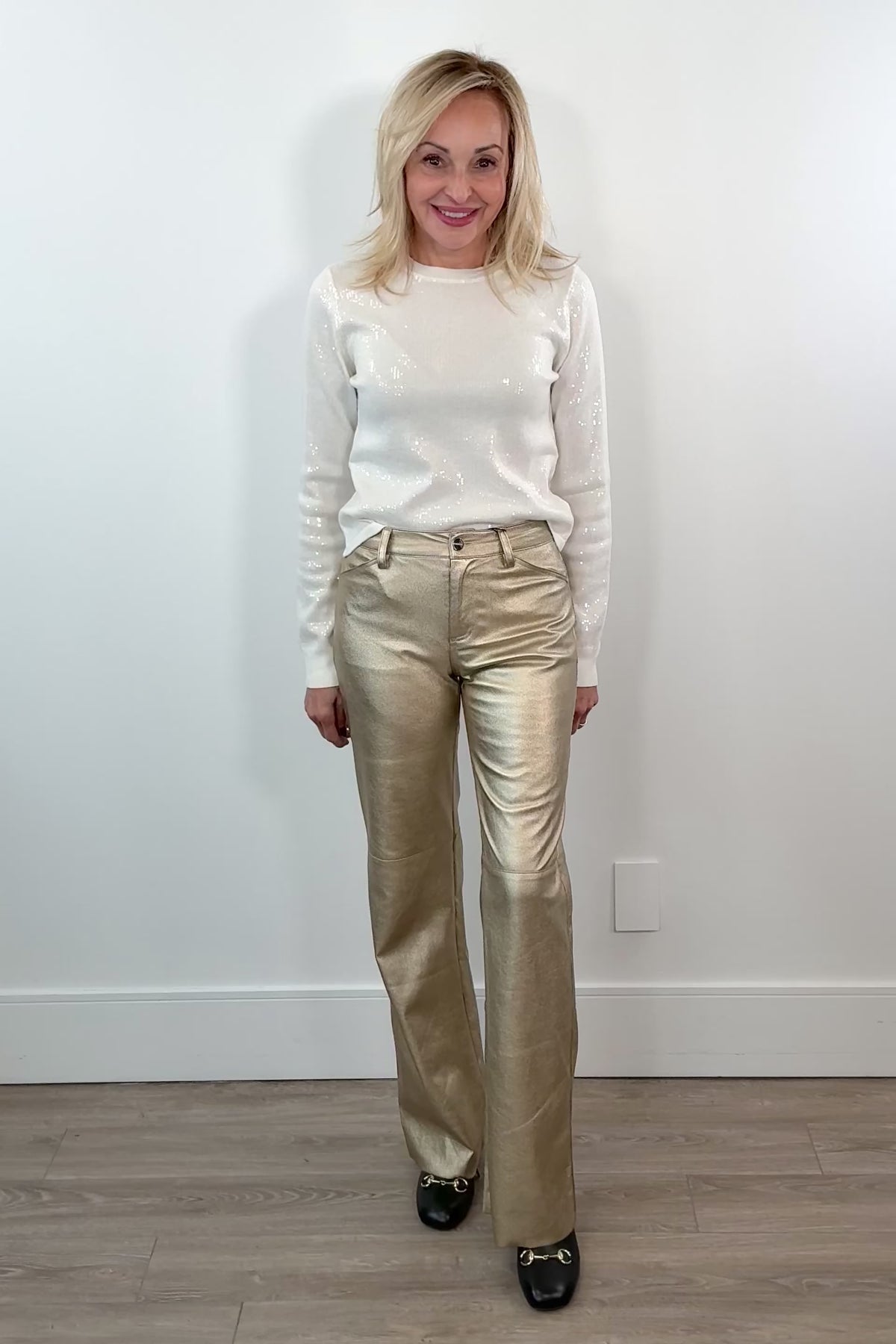 video of woman wearing gold metallic pants against a white wall.