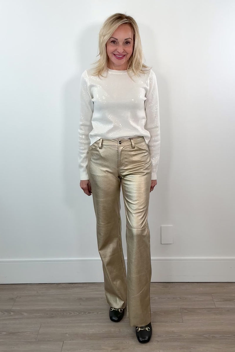 video of woman wearing gold metallic pants against a white wall.