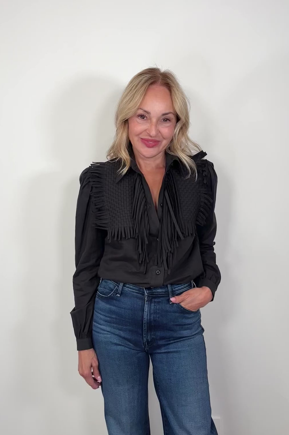Video of a woman wearing a black long sleeve collared blouse with fringes 