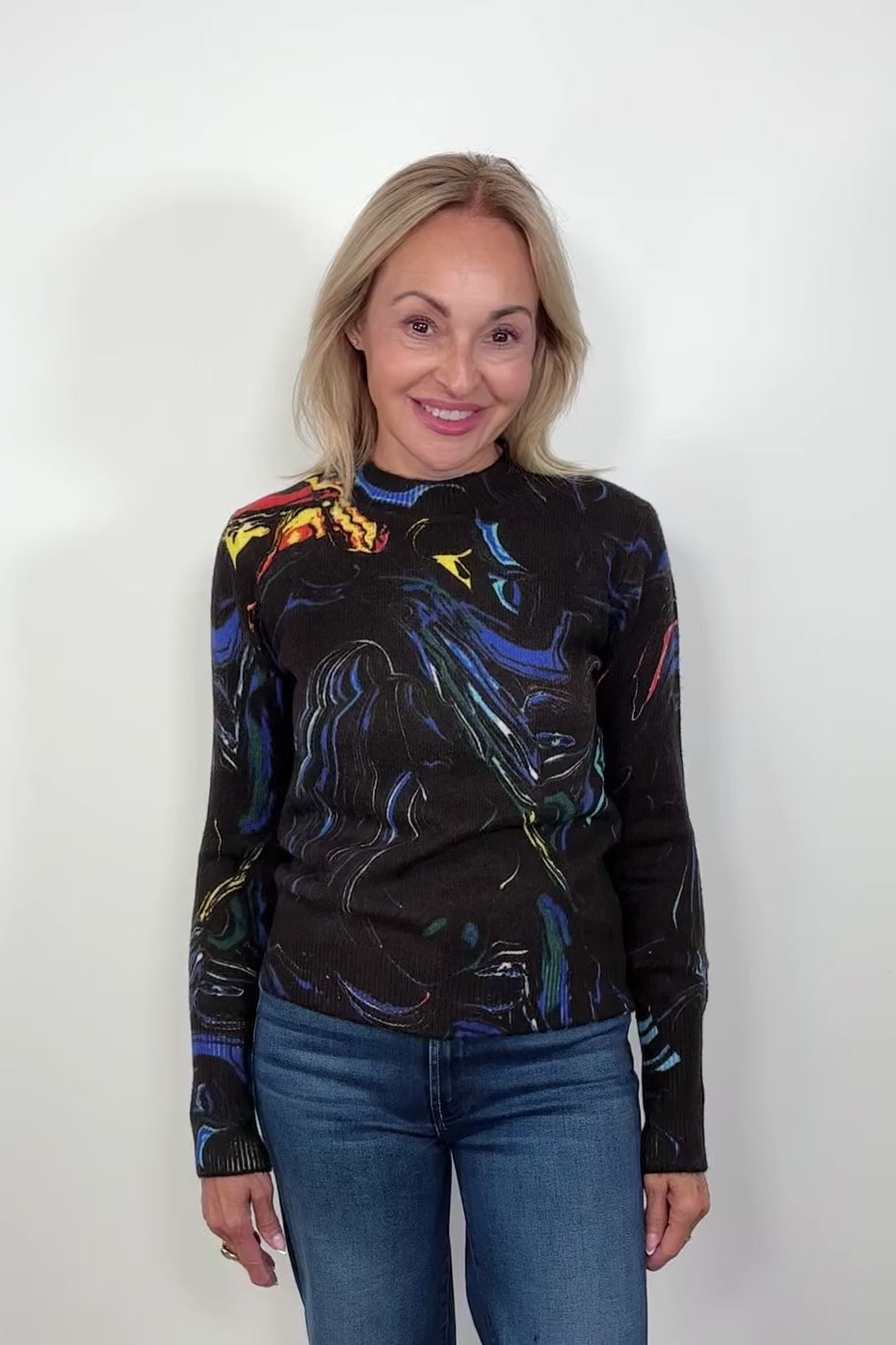 Woman wearing a black long-sleeve sweater with colorful abstract design against a white background