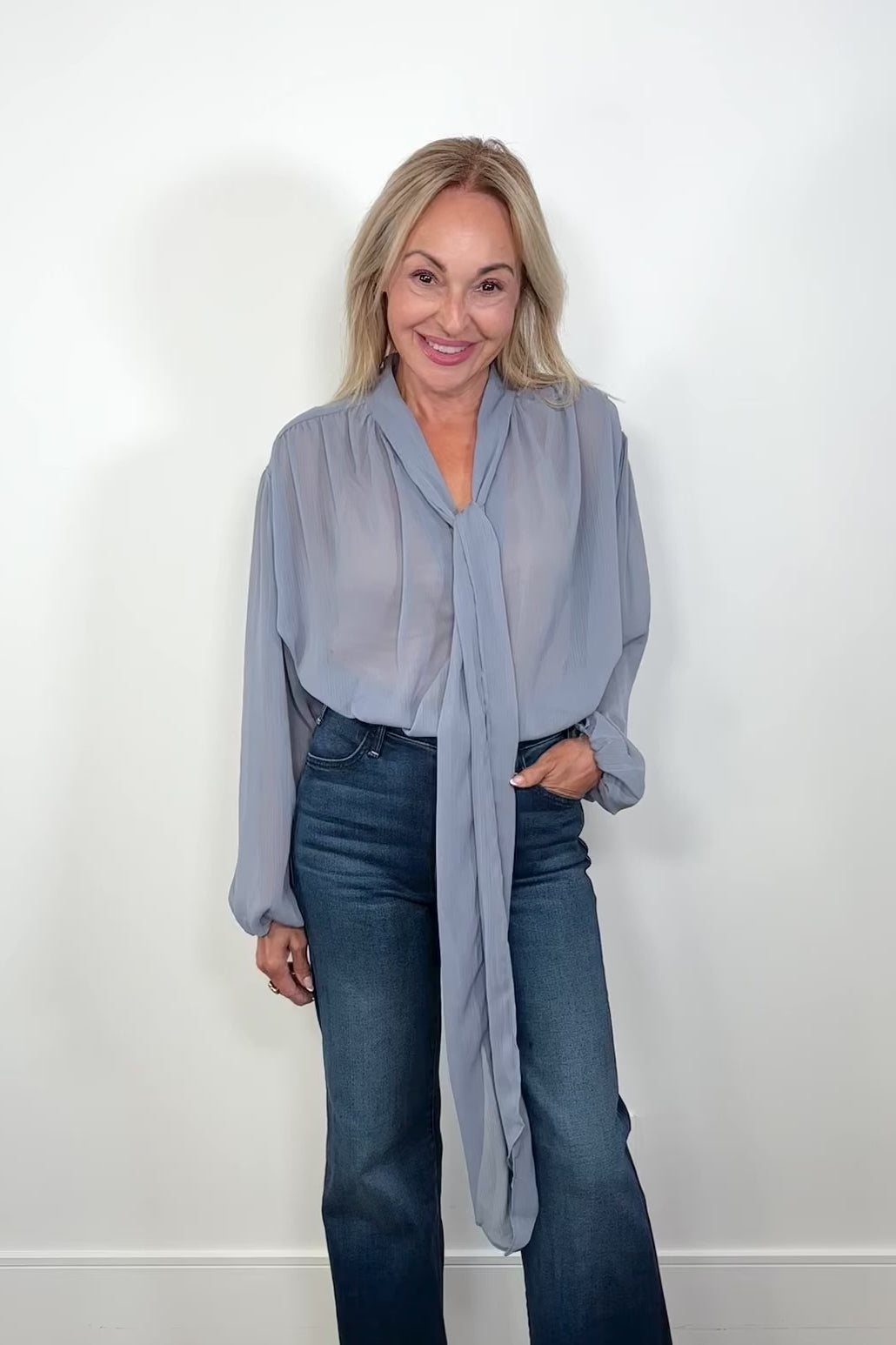 Video of woman wearing a thin blue blouse tucked in turning around to show the back