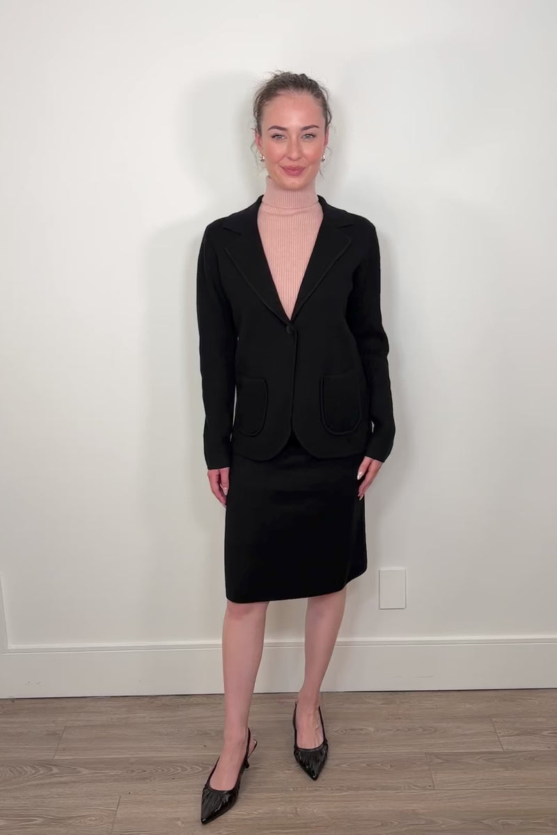 Video of woman wearing a matching black knitted blazer and skirt with heels and a pink turtleneck tank top