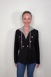 Video of woman wearing a black jacket that includes a detachable gray hoodie against a plain background
