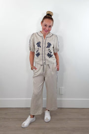 Video of a woman wearing cream linen drawstring pants with contrast embroidery along the sides