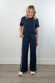 video of woman wearing navy wide leg track pants with white stripes going down the side leg and a drawstring waistband