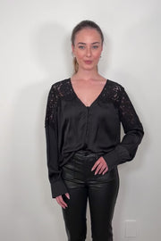 Video of a woman wearing a black long sleeve satin blouse with lace detailing on the shoulders tucked in