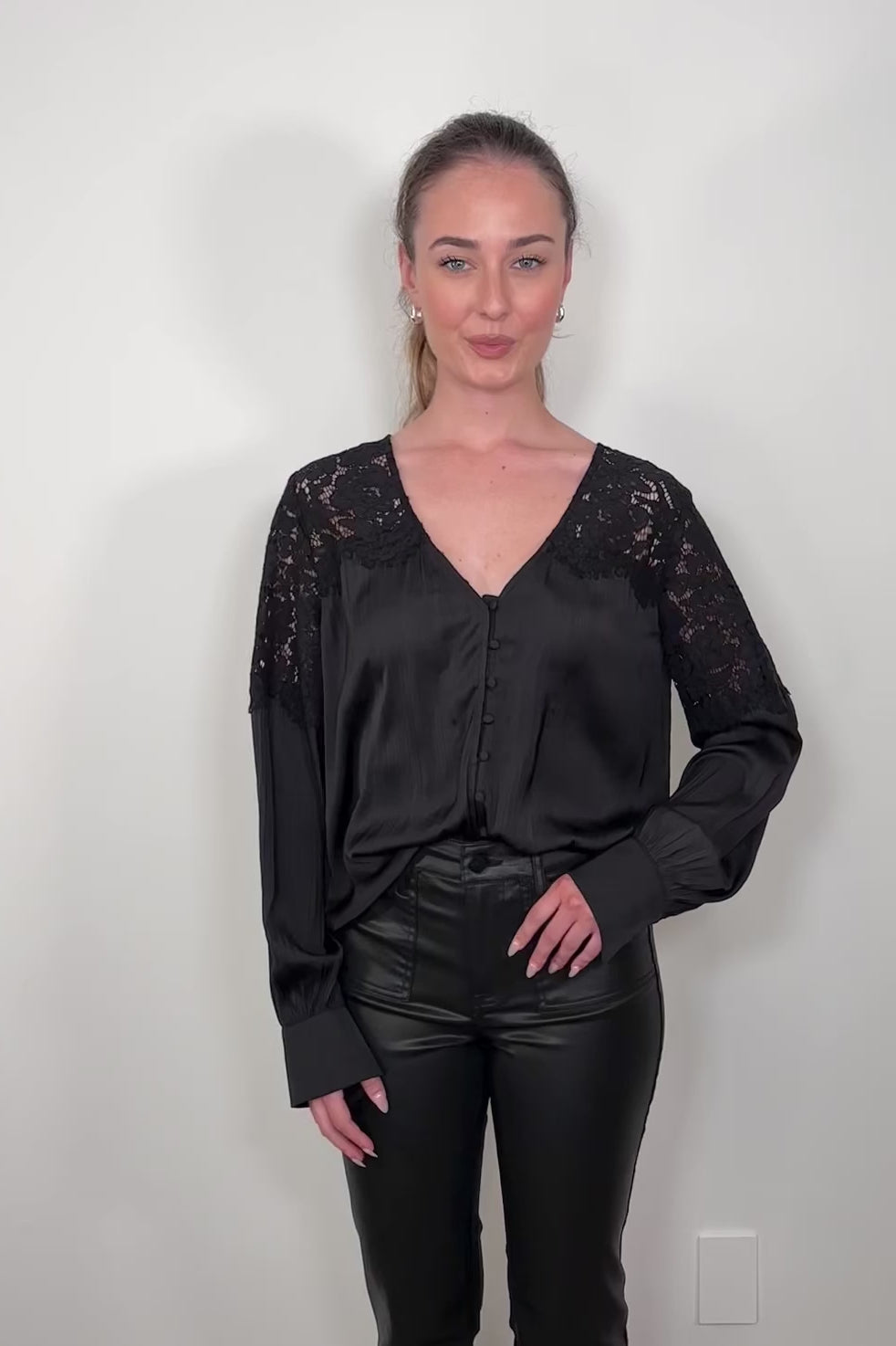 Video of a woman wearing a black long sleeve satin blouse with lace detailing on the shoulders tucked in