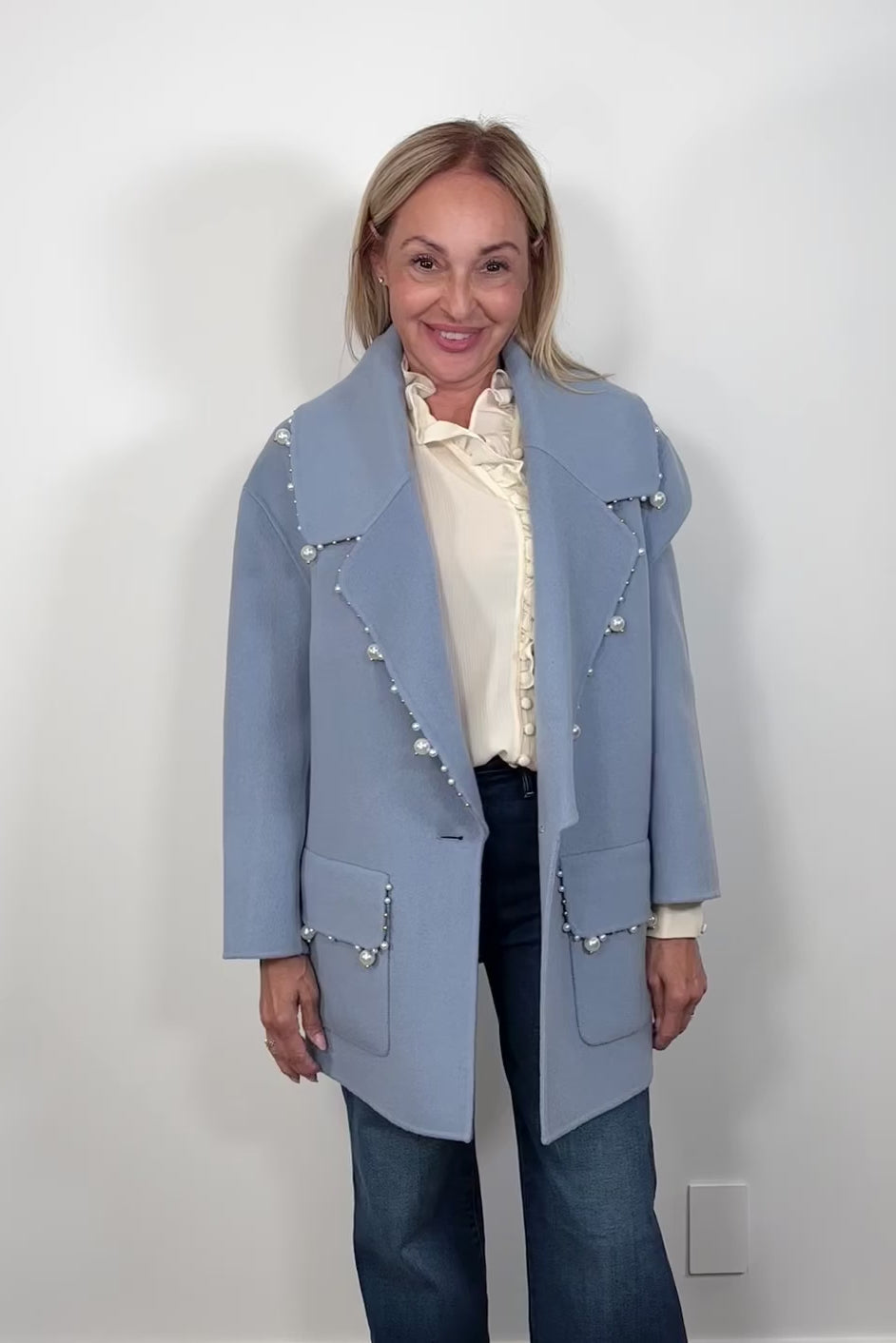 Video of woman wearing an oversized blue blazer with pearl detailing on the trim paired with a off white blouse and jeans