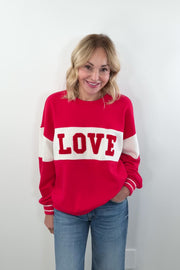 video of woman wearing a red and off white pullover with the word "LOVE"written in chenille 