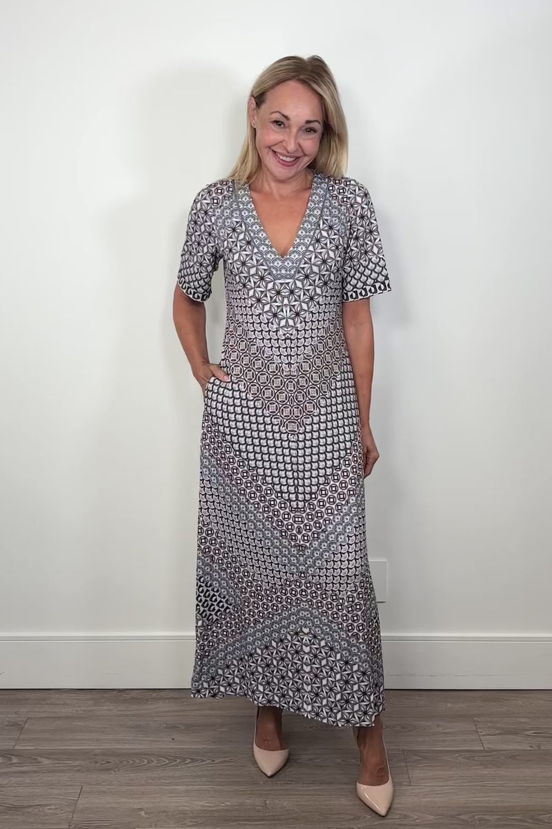 Video of a woman wearing a black and blue pattern jersey midi dress turning around to show the back 