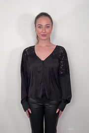 video of a woman wearing a black long sleeve satin blouse with lace detailing on the shoulders untucked