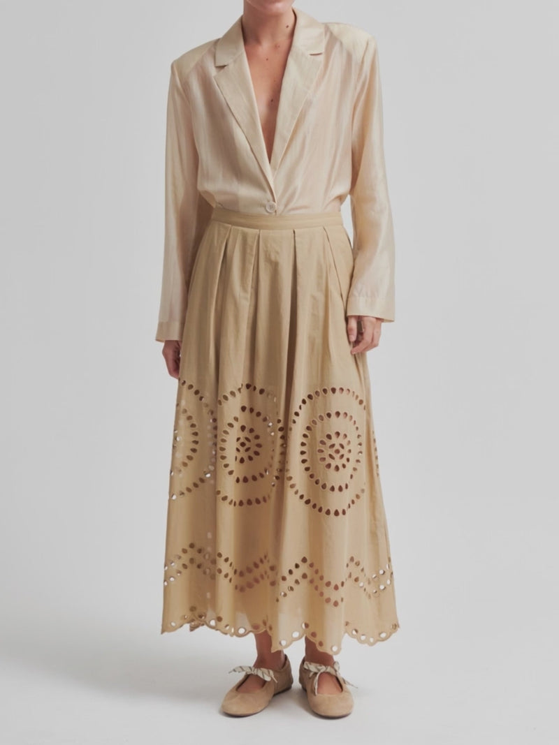 Woman wearing a beige midi skirt with embroidery details and concealed side pockets