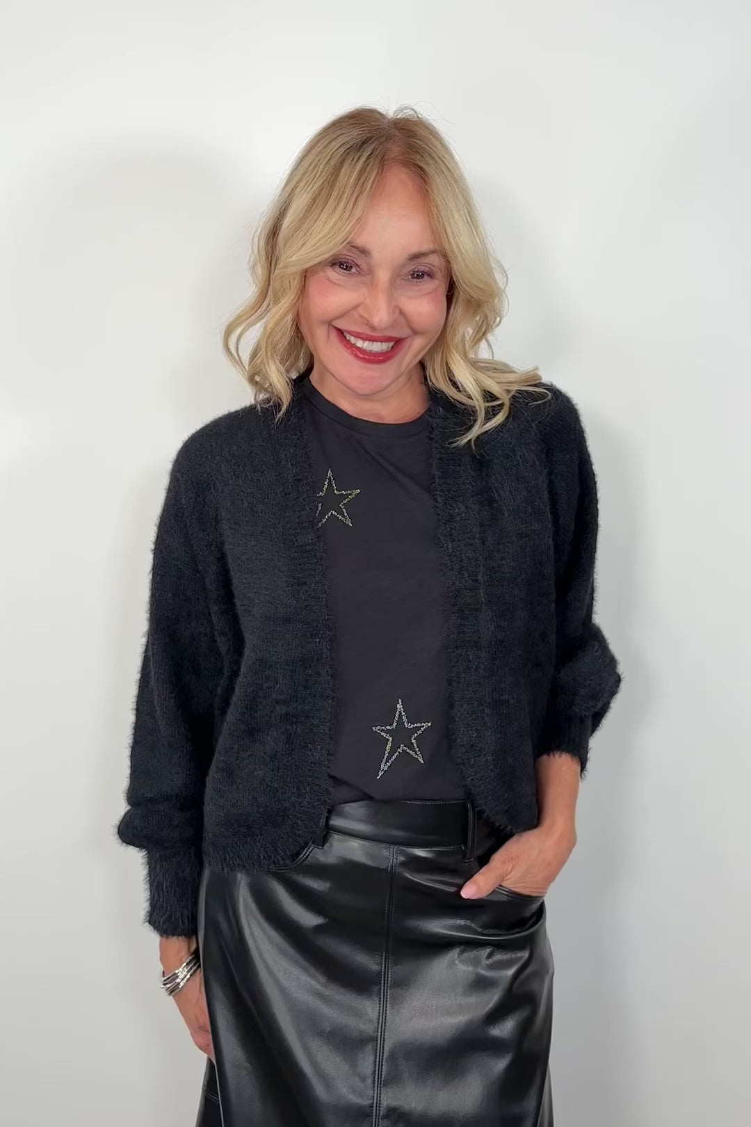 video of a woman wearing. a black shrug cardigan over a star print tee