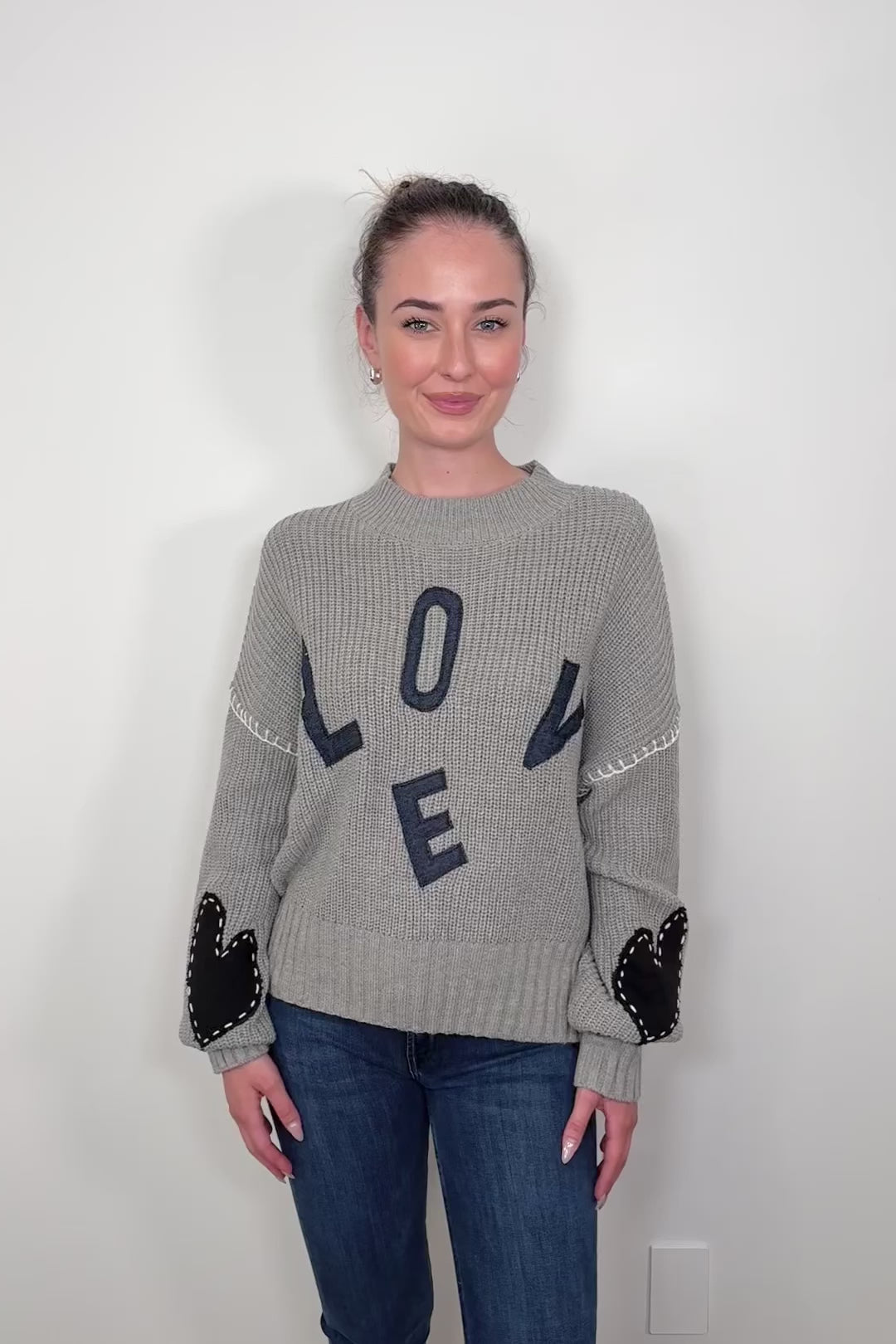 Video of woman wearing a gray sweater with letter spelling love, hearts in the elbows with whipstitch detailing