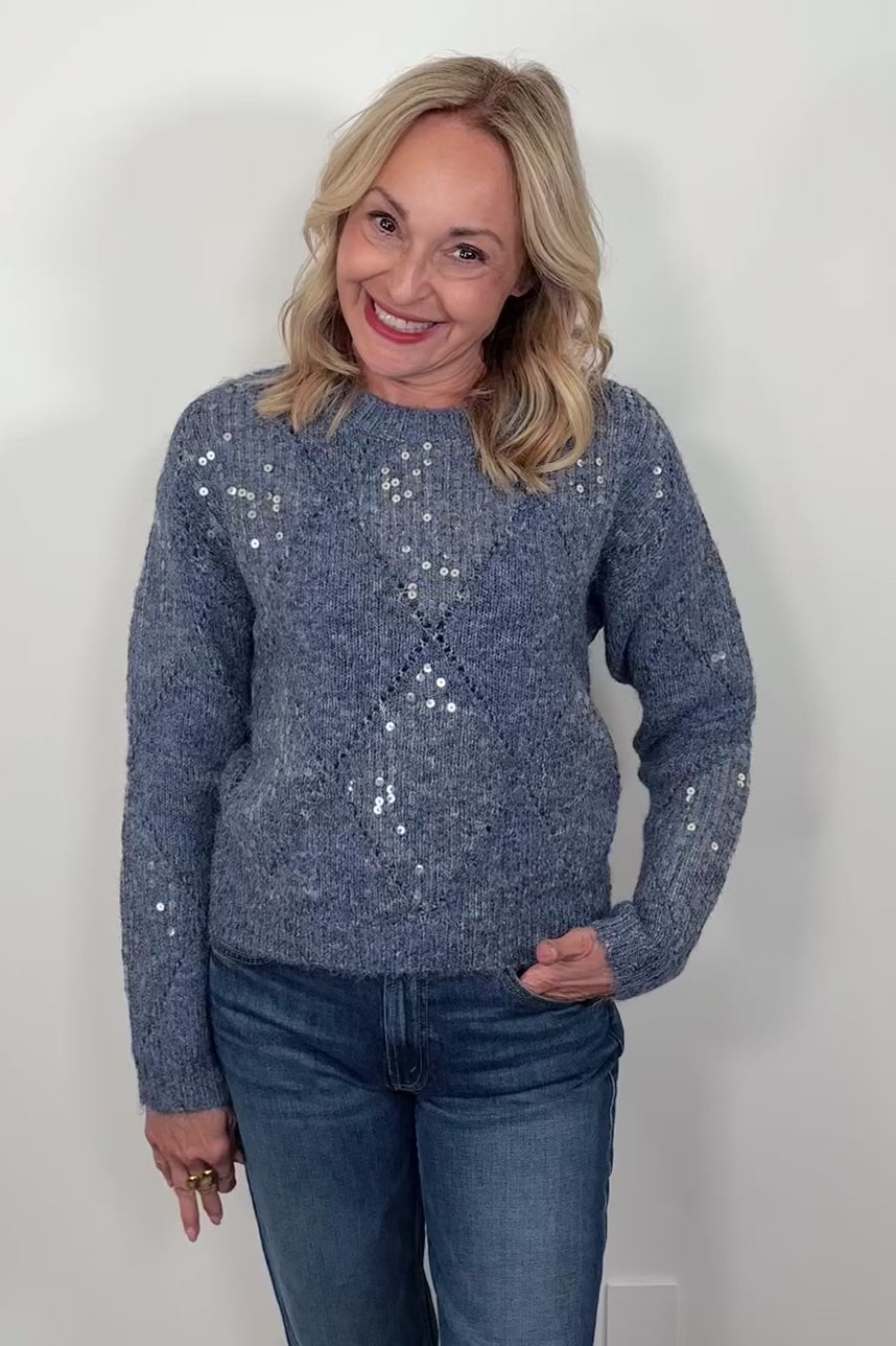 Video of a woman wearing a blue diamond sequin pattern sweater against a white background