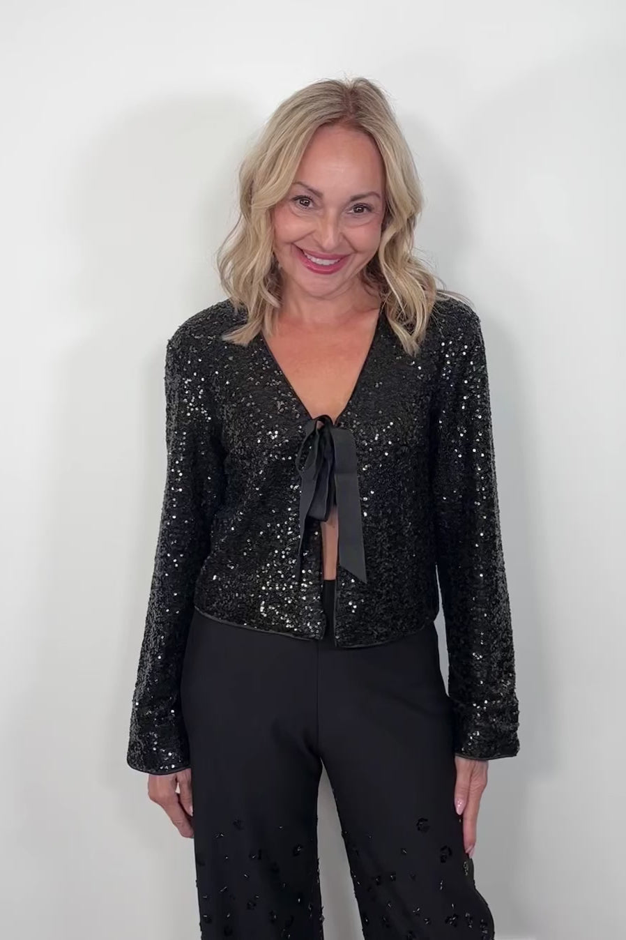 video of a w oman wearing a black sequin cardigan with a bow tie against a white background
