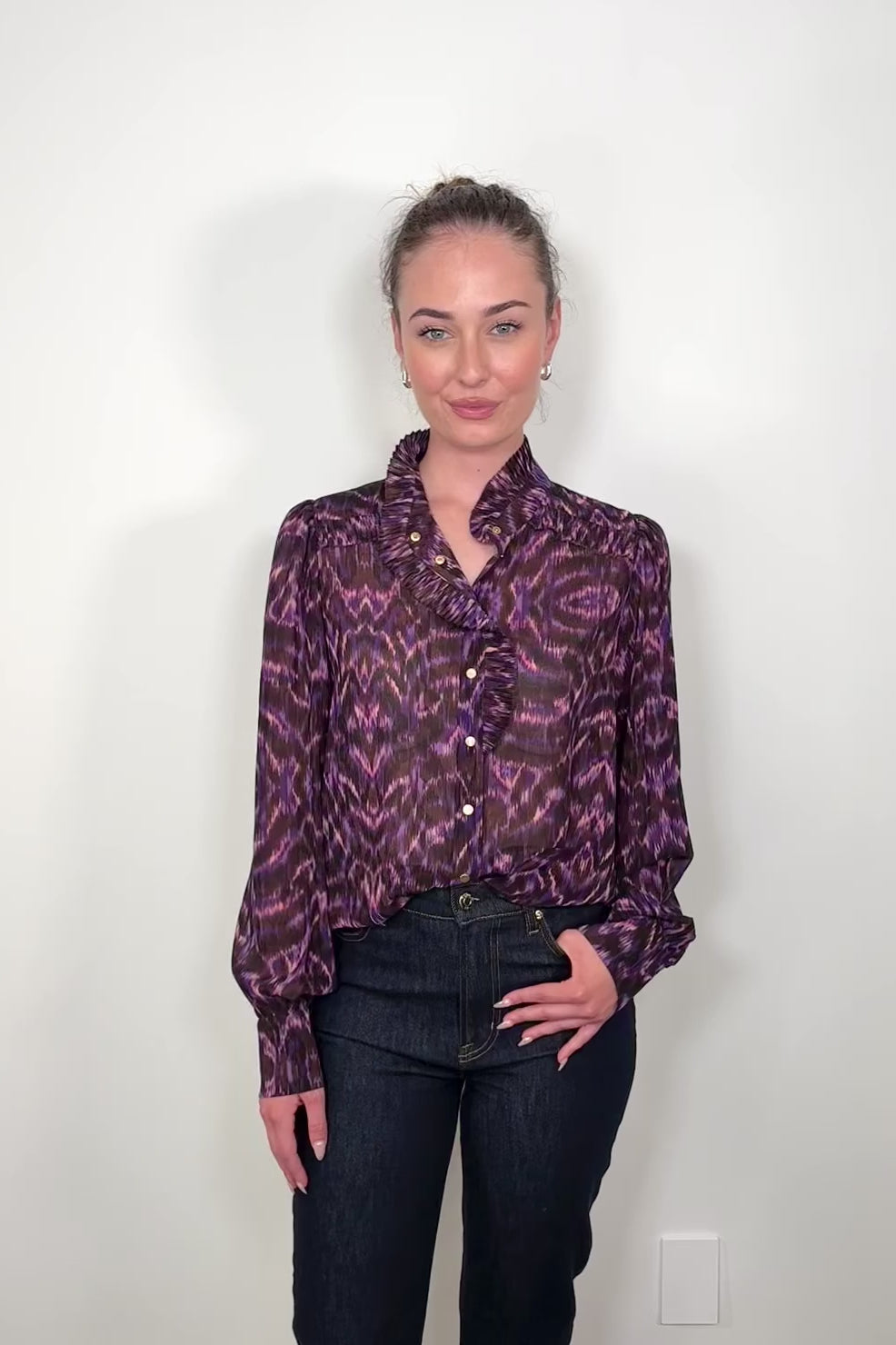 Video of a woman wearing a violet sheer printed blouse with ruffles tucked in
