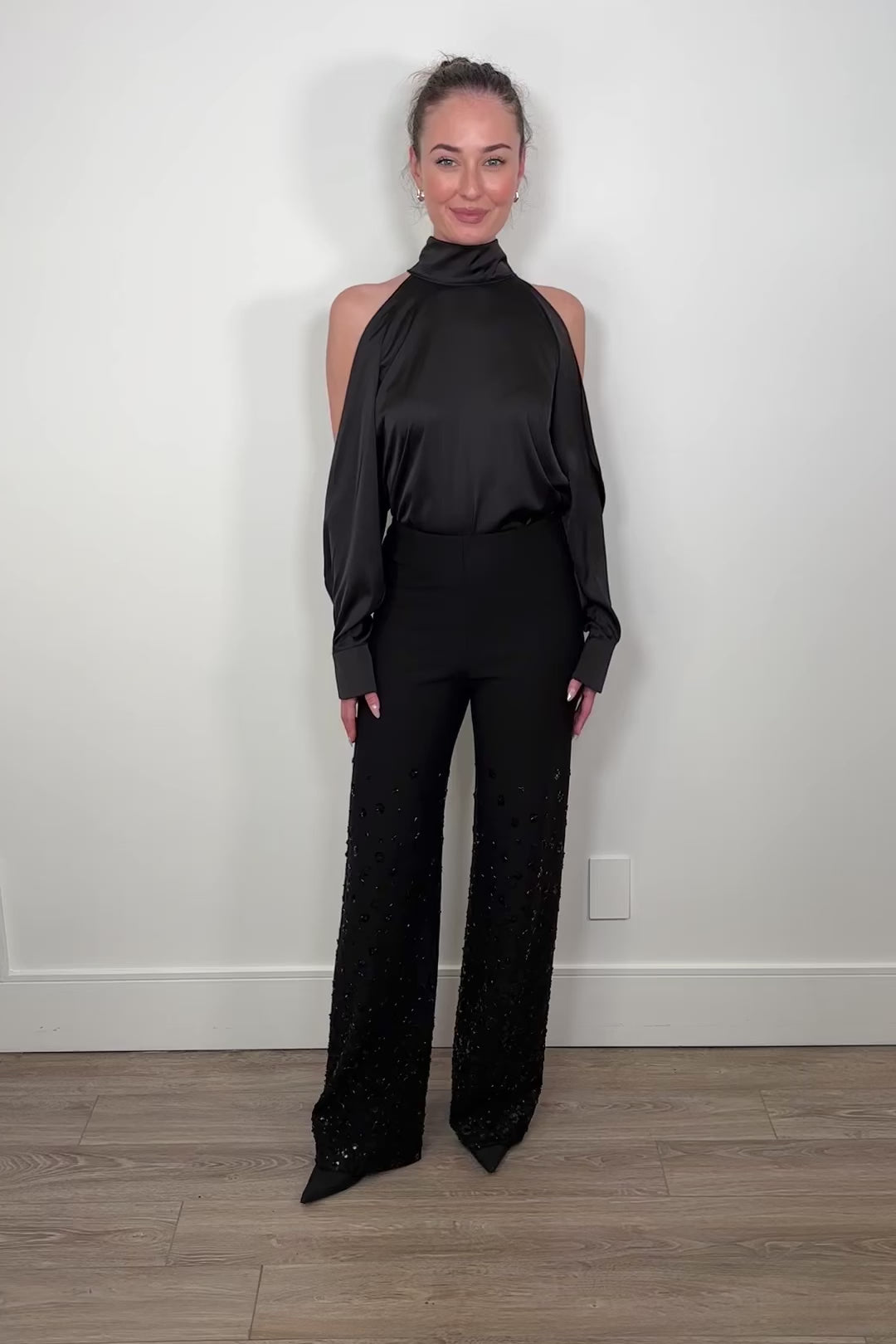 Video of a woman wearing a black high-neck top and a floral embellished relaxed fit black pants