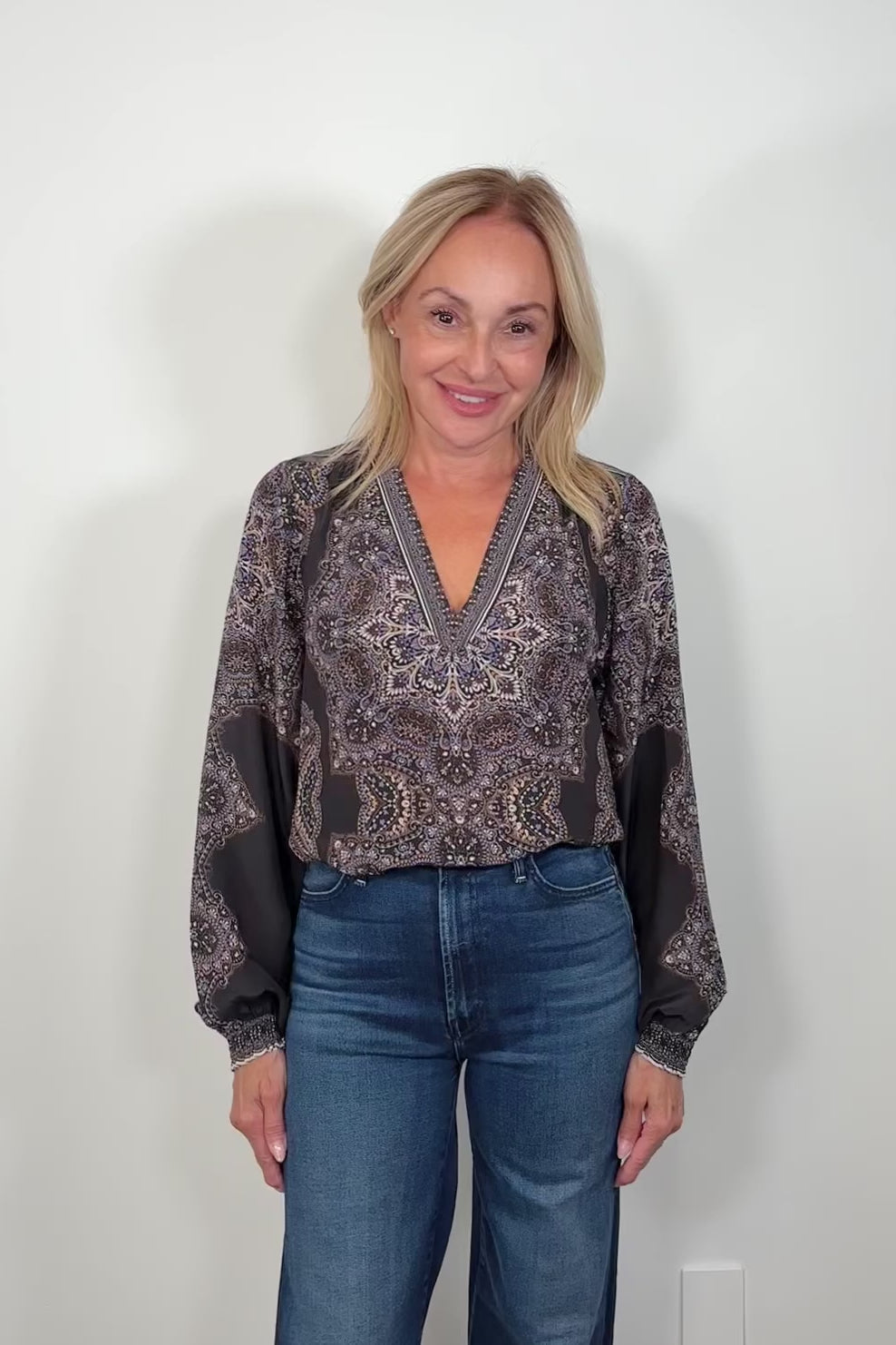 Video of woman wearing a cuffed blouson sleeved patterned black blouse tucked in