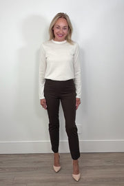 Video of woman wearing dark brown fitted pants with nude heels against a white wall turning around to show the back.