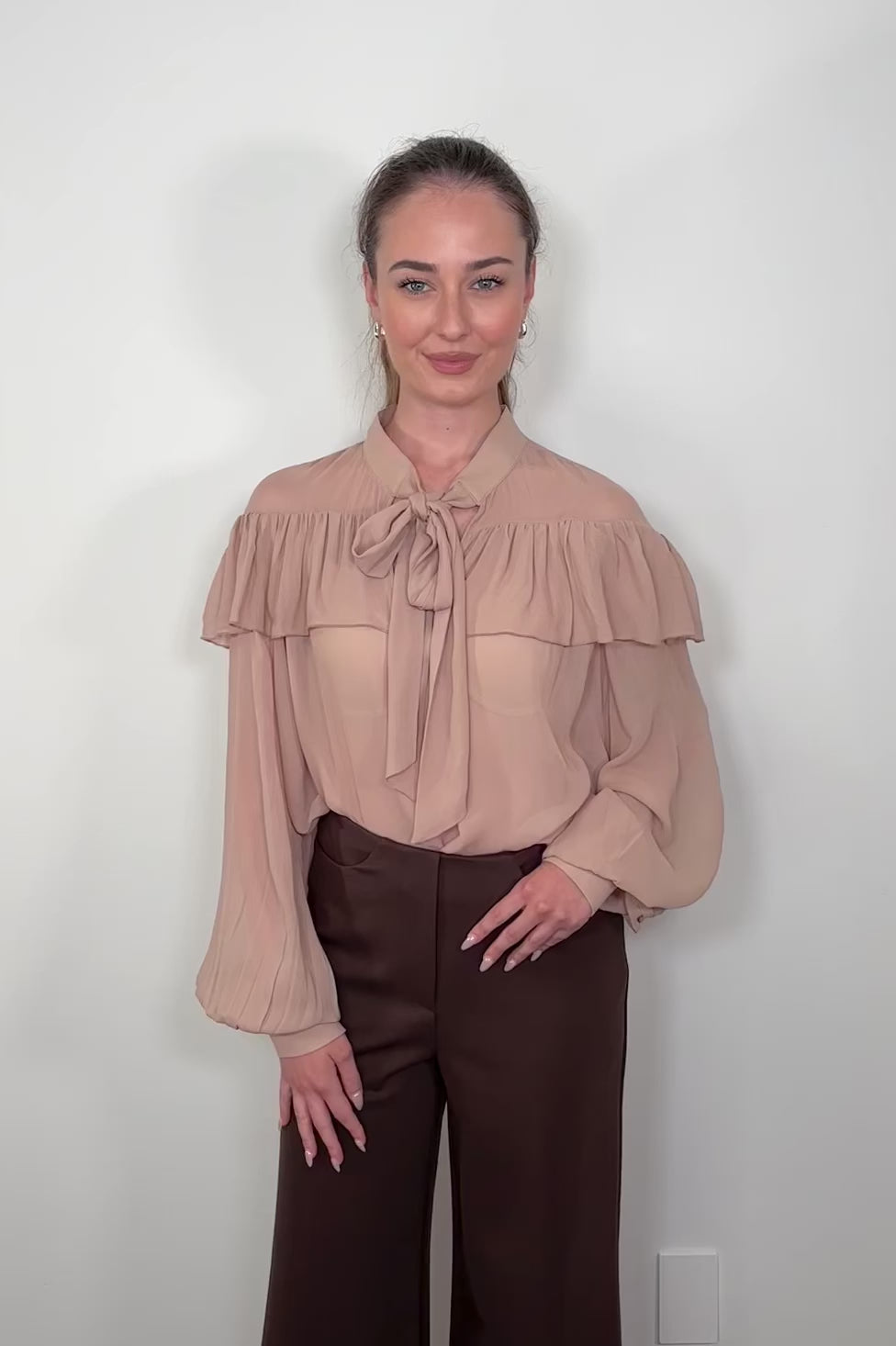 Video of woman wearing a nude coloured sheer ruffle tie neck blouse