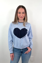 video of a woman wearing a light blue sweater with a navy heart design and "XOXO" embroidered 