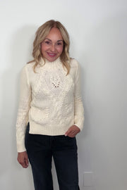 Video of a woman wearing a cream-colored cable knit sweater 