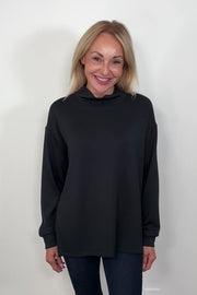 Video of a woman wearing a black boxy turtleneck top turning around to show the back