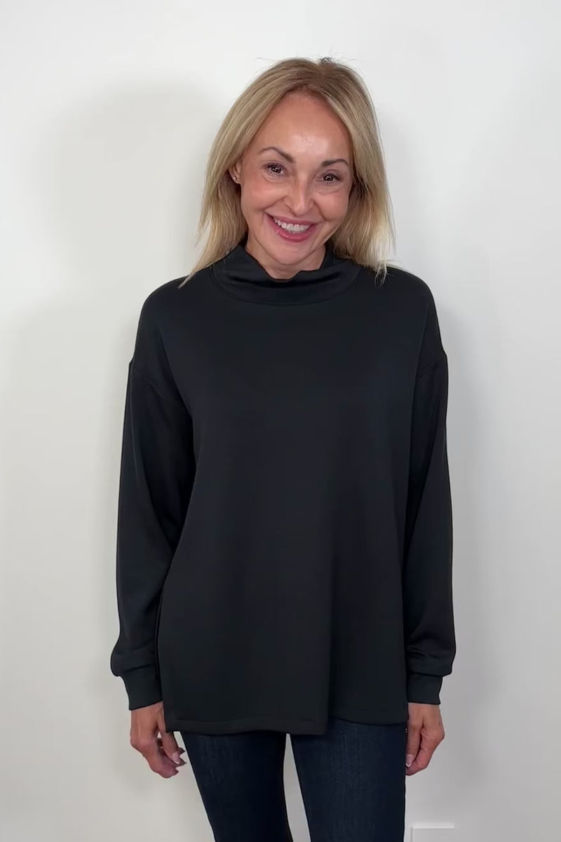 Video of a woman wearing a black boxy turtleneck top turning around to show the back