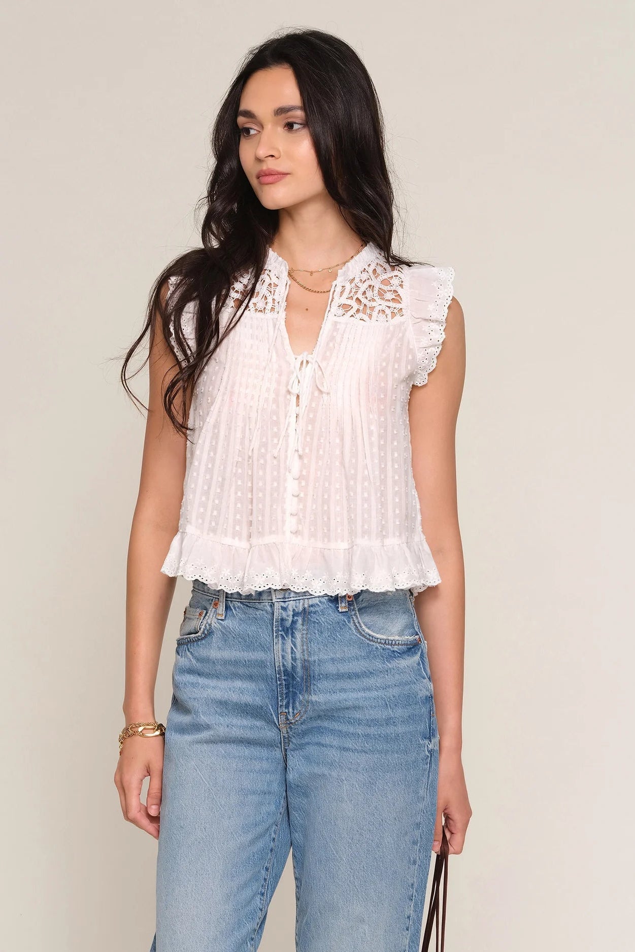 woman wearing a white sleeveless blouse with lace yoke detailing, ruffled trim, and a button-front design paired with light wash jeans, front