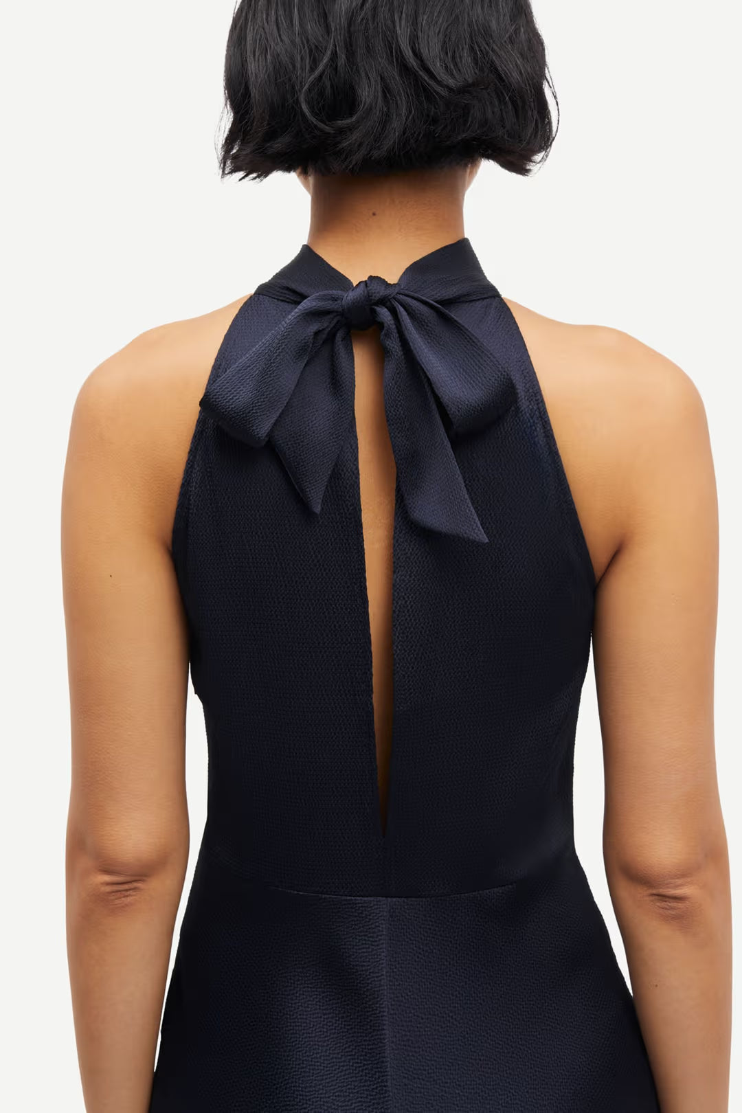 Woman wearing a navy sleeveless halter-neck midi dress with a fitted bodice and flared skirt, back detail view
