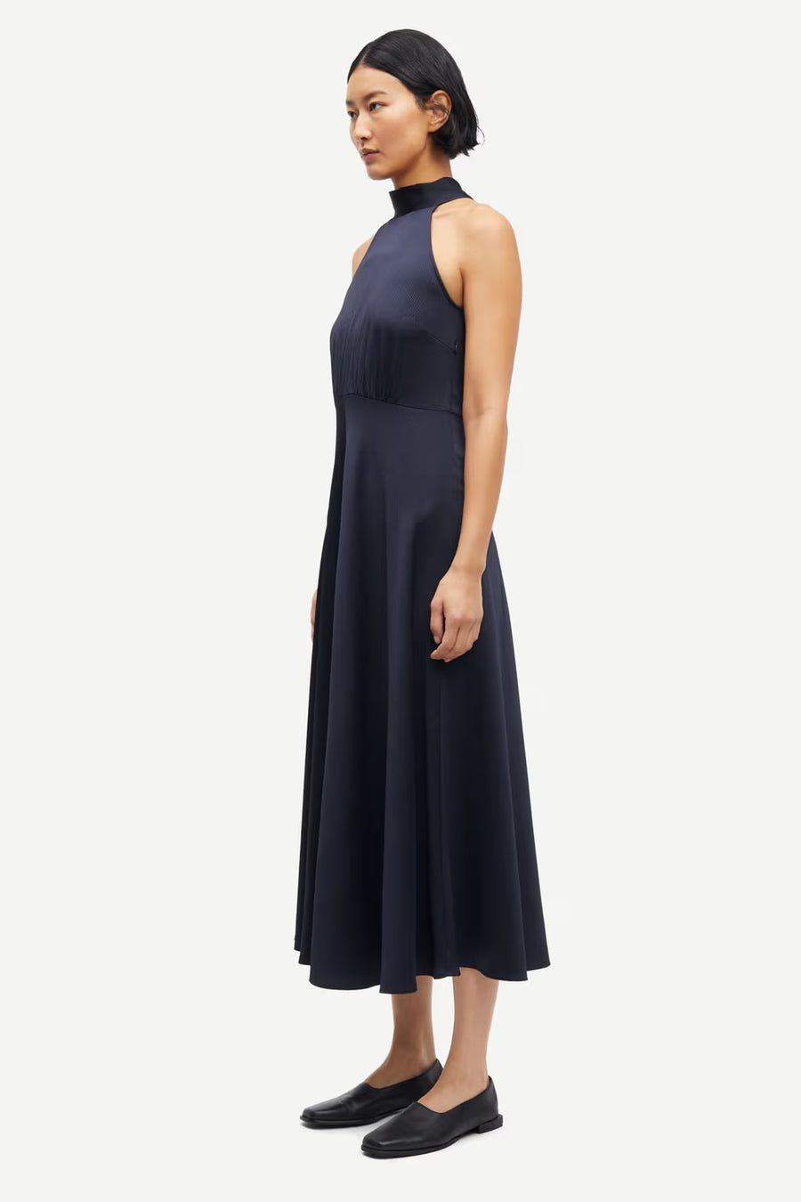 Woman wearing a navy sleeveless halter-neck midi dress with a fitted bodice and flared skirt, side view