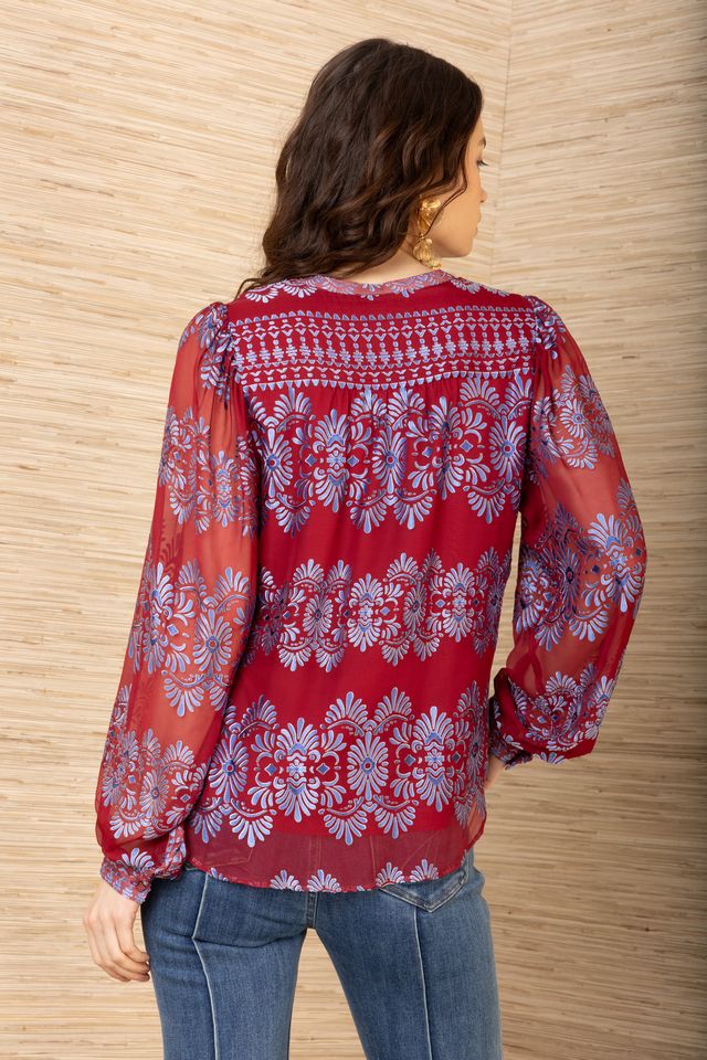 Back view of woman wearing a red background and blue patterned long sleeve blouse